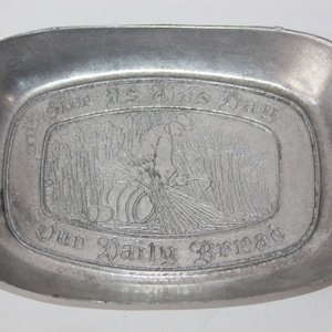 May include: A silver metal bread tray with an engraved image of a person harvesting wheat and the text "Give Us This Day Our Daily Bread".