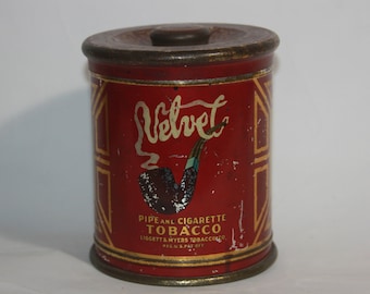Può includere: Scatola di latta rossa con coperchio dorato e bordi dorati. La scatola ha un'immagine di una pipa e la parola "Velvet" in un carattere stilizzato. Il testo sulla scatola recita "Pipe and Cigarette Tobacco Liggett & Myers Tobacco Co. Reg. U.S. Pat. Off."