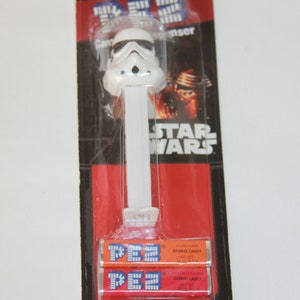 May include: A white Star Wars Stormtrooper Pez dispenser with three packs of Pez candy: orange, cherry, and cherry. The packaging is red and black with the Star Wars logo. Total candy net weight: 0.87 oz (24.7 g).
