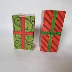 May include: A set of two ceramic salt and pepper shakers shaped like wrapped presents. One shaker is green with red ribbon and the other is red with green ribbon.