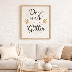 Puede incluir: Un cuadro rectangular con marco de madera clara que presenta el texto negro "Dog HAIR is my Glitter" centrado sobre un fondo blanco, decorado con huellas de patas doradas brillantes y peque&ntilde;as estrellas alrededor de las letras.
