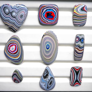 May include: Nine polished stones with distinctive, colourful, swirling patterns. Shapes include a heart, square, oval, and teardrop. The stones feature a variety of colours, including blue, red, yellow, and black, creating a striking visual effect.
