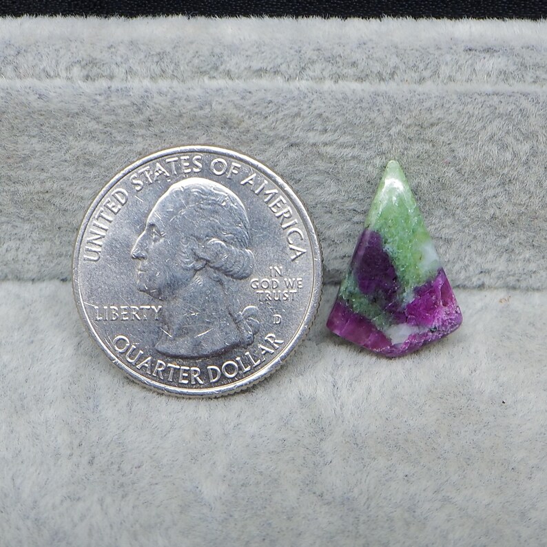 May include: A triangular-shaped gemstone with a mix of green, white, and magenta colors. A U.S. quarter coin is next to the gemstone for size comparison. The gemstone has a polished surface and a natural, organic appearance.