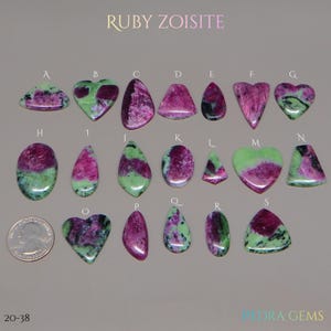 May include: A collection of ruby zoisite gemstones in various shapes, including hearts, ovals, and teardrops. The stones display a mix of green and magenta colors. The image includes a quarter for size comparison.