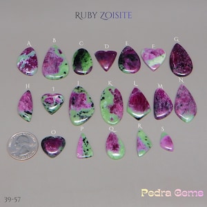 May include: A collection of ruby zoisite gemstones in diverse shapes, such as teardrop, oval, and heart. The stones display a blend of pink, green, and black hues. The text "RUBY ZOISITE" and "Pedra Gems" are visible.