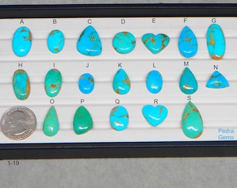 May include: A collection of nineteen turquoise gemstones in various shapes, including oval, teardrop, and heart. The stones are displayed in a black tray, with a quarter for size comparison. Some stones have brown matrix patterns.