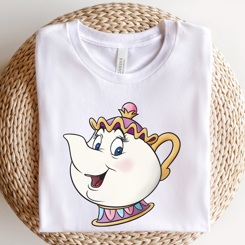 May include: White t-shirt with a cartoon image of Mrs. Potts, the teapot character from Beauty and the Beast. She has a pink and yellow hat and a blue and white trim around her base.