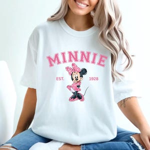 May include: White t-shirt with a pink Minnie Mouse graphic and the text "MINNIE EST. 1928".