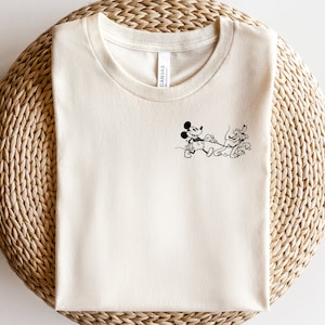 Könnte beinhalten: Ein weißes T-Shirt mit einer Schwarzweißillustration von Mickey Mouse und Pluto. Die Illustration zeigt Mickey Mouse mit einem Pinsel und Pluto mit einem Farbeimer.