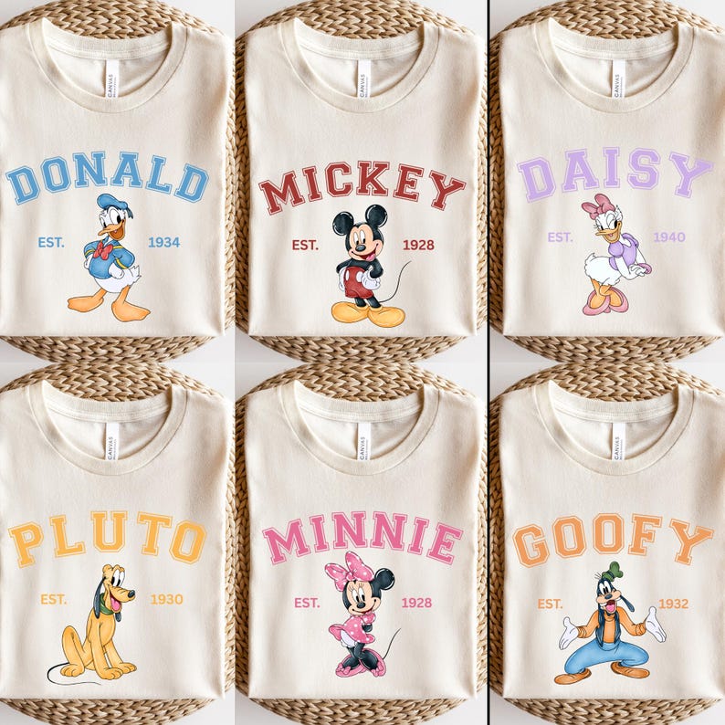 May include: Six cream-colored t-shirts with different Disney character designs. Each shirt features a character's name in a colorful, varsity-style font, along with the character's established year. The characters featured are Donald Duck, Mickey Mouse, Daisy Duck, Pluto, Minnie Mouse, and Goofy.