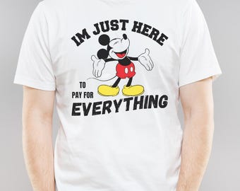 May include: White t-shirt featuring a smiling Mickey Mouse graphic with the text "IM JUST HERE TO PAY FOR EVERYTHING" in black. Mickey is depicted in his classic red shorts, yellow shoes, and white gloves.