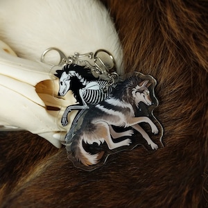 Peut inclure: Un porte-cl&eacute;s argent&eacute; avec un charme de squelette de loup noir et blanc et un charme de loup brun et blanc. Les charmes sont attach&eacute;s &agrave; une cha&icirc;ne argent&eacute;e avec un anneau argent&eacute;.