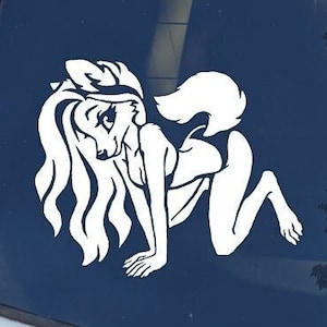 May include: White vinyl sticker of a cartoon wolf woman with long hair and a tail, in a crouching pose. The sticker is on a blue car window. The text "Mugwump Studios" is in the top right corner of the image.