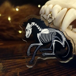 Peut inclure: Un porte-cl&eacute;s en acrylique noir et blanc repr&eacute;sentant un loup squelette avec un contour de fourrure noir. Le porte-cl&eacute;s est suspendu &agrave; une cha&icirc;ne argent&eacute;e.