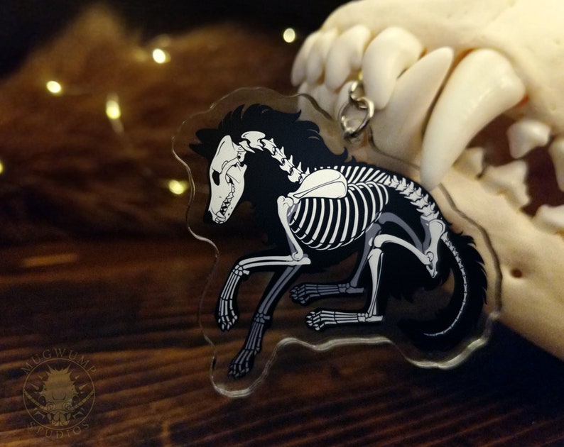 Peut inclure: Un porte-cl&eacute;s en acrylique noir et blanc repr&eacute;sentant un loup squelette avec un contour de fourrure noir. Le porte-cl&eacute;s est suspendu &agrave; une cha&icirc;ne argent&eacute;e.