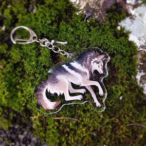 Peut inclure: Un porte-cl&eacute;s en acrylique transparent repr&eacute;sentant un loup de dessin anim&eacute; avec une fourrure grise, blanche et brune. Le loup est couch&eacute;, la t&ecirc;te tourn&eacute;e sur le c&ocirc;t&eacute;. Le porte-cl&eacute;s est attach&eacute; &agrave; une cha&icirc;ne et un anneau en m&eacute;tal argent&eacute;.