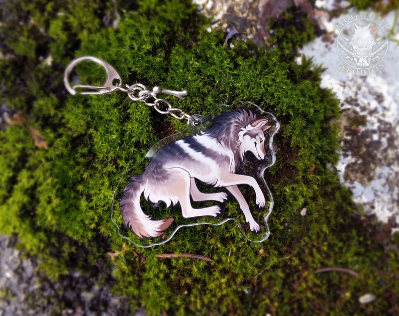 Peut inclure: Un porte-cl&eacute;s en acrylique transparent repr&eacute;sentant un loup de dessin anim&eacute; avec une fourrure grise, blanche et brune. Le loup est couch&eacute;, la t&ecirc;te tourn&eacute;e sur le c&ocirc;t&eacute;. Le porte-cl&eacute;s est attach&eacute; &agrave; une cha&icirc;ne et un anneau en m&eacute;tal argent&eacute;.