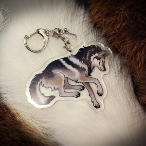 Peut inclure: Un porte-cl&eacute;s en acrylique transparent repr&eacute;sentant un loup gris et blanc avec une fourrure noire sur la t&ecirc;te. Le porte-cl&eacute;s est dot&eacute; d'un anneau et d'une cha&icirc;ne en m&eacute;tal argent&eacute;.
