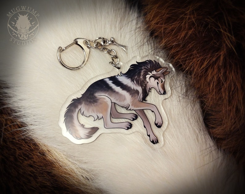 Peut inclure: Un porte-cl&eacute;s en acrylique transparent repr&eacute;sentant un loup gris et blanc avec une fourrure noire sur la t&ecirc;te. Le porte-cl&eacute;s est dot&eacute; d'un anneau et d'une cha&icirc;ne en m&eacute;tal argent&eacute;.