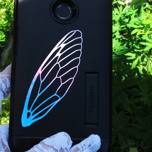 May include: A black phone case with a blue and pink insect wing design. The text "#WeRide" is on the side of the case.
