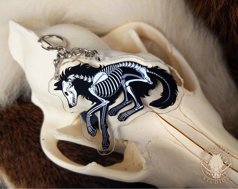 Peut inclure: Un porte-cl&eacute;s en acrylique noir et blanc repr&eacute;sentant un loup squelette avec une silhouette noire. Le porte-cl&eacute;s est attach&eacute; &agrave; une cha&icirc;ne argent&eacute;e.
