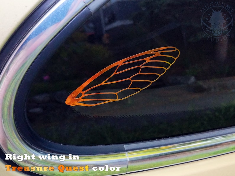May include: A close-up of a car window with a gold-colored cicada wing decal. The decal is a right wing and is in the "Treasure Quest" color. The decal is on the back window of a car.