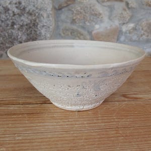May include: A white ceramic bowl with a blue and white floral design. The bowl is slightly wider at the top and tapers down to a rounded bottom.