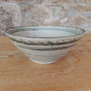 May include: A small, white ceramic bowl with a grey and black striped design. The bowl is sitting on a wooden surface.