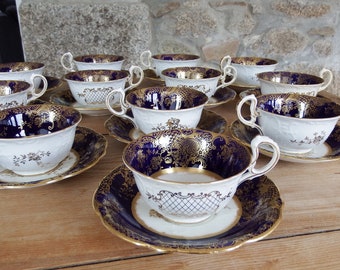 May include: A set of 12 teacups and saucers with a cobalt blue and gold design. The cups and saucers have a delicate floral pattern and a scalloped edge.