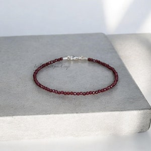 Puede incluir: Un brazalete delicado hecho con pequeñas cuentas de granate facetadas y un cierre de plata.