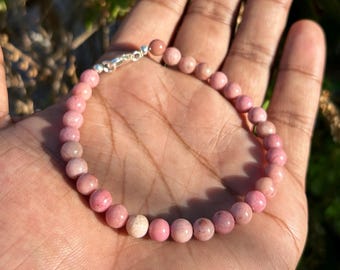 May include: A pink gemstone bracelet with a silver clasp. The bracelet is made of small, round beads.