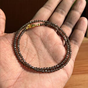 May include: A delicate necklace featuring small, faceted, smoky quartz beads. The necklace is a double strand design, secured with a gold-coloured clasp. The beads have a subtle, shimmering quality.