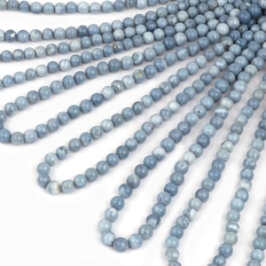 May include: A strand of light blue gemstone beads. The beads are round and smooth, and they are strung on a clear thread. The beads are arranged in a fan shape, and they are all the same size.