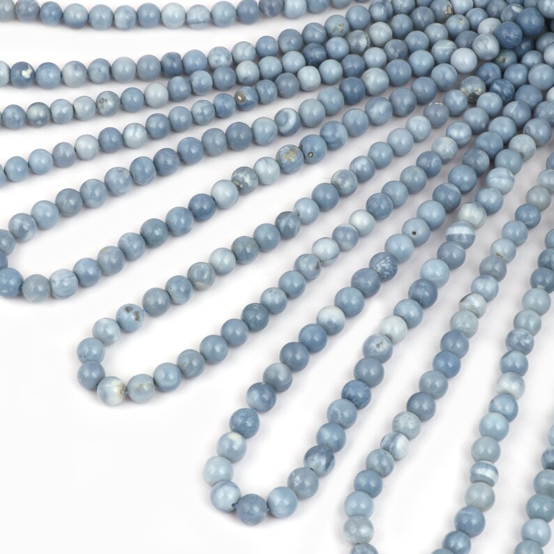 May include: A strand of light blue gemstone beads. The beads are round and smooth, and they are strung on a clear thread. The beads are arranged in a fan shape, and they are all the same size.