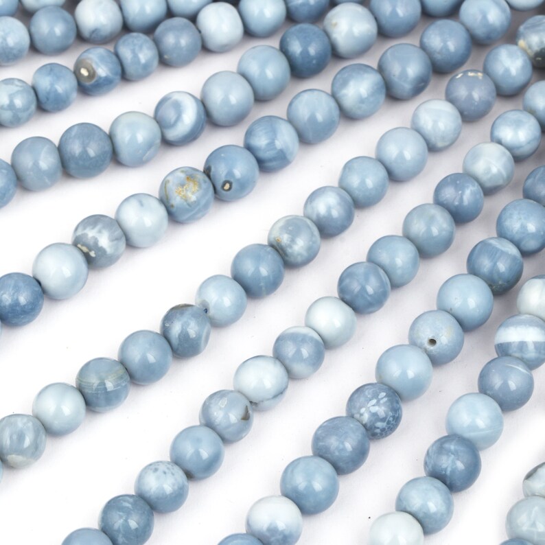 May include: A strand of light blue opal beads, each bead is round and smooth. The beads are arranged in rows, creating a pattern of overlapping circles.