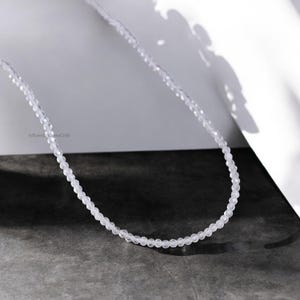 Op de afbeelding: Een delicate ketting gemaakt van kleine, heldere, gefacetteerde kralen. De ketting ligt op een wit oppervlak.