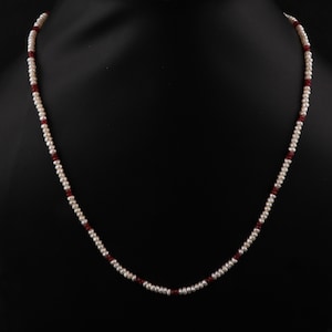 May include: A white pearl necklace with small red beads interspersed throughout.