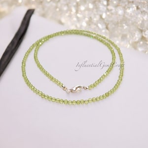 May include: A delicate green peridot necklace with a silver clasp. The necklace is made of small, round beads and is approximately 18 inches long.