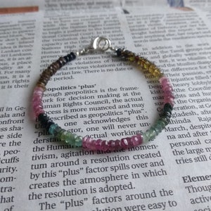 May include: A multi-coloured gemstone bracelet with a silver clasp. The bracelet features pink, green, black and gold beads.