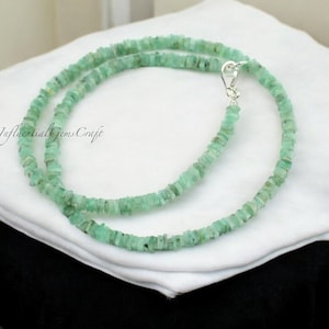 May include: A green emerald gemstone necklace with a silver clasp. The necklace is made of small, square-shaped beads.