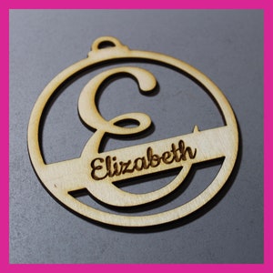 May include: A wooden Christmas bauble with the letter "E" and the name "Elizabeth" engraved on it.