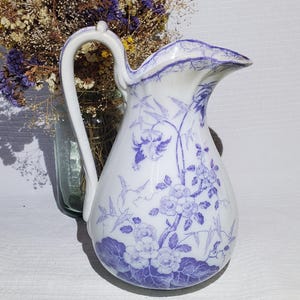 May include: White ceramic pitcher with a curved handle and a spout. The pitcher is decorated with a blue floral pattern and bird motifs. The pitcher is likely used for serving beverages.