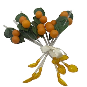 May include: A set of orange and green cocktail stirrers with orange-shaped tops and spoon-shaped bottoms. The stirrers are tied together with a white ribbon.