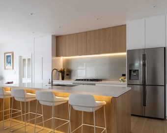 May include: A modern kitchen with white cabinets, a stainless steel refrigerator, and a kitchen island with white bar stools. The island has a white countertop and a wood base.