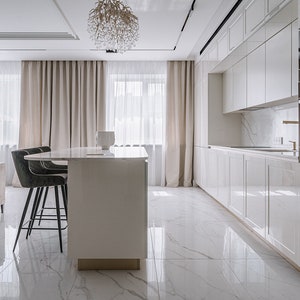Op de afbeelding: Een wit keuken eiland met een wit aanrecht en twee zwarte barstoelen. Het eiland bevindt zich in een moderne keuken met witte kasten en een marmeren vloer.
