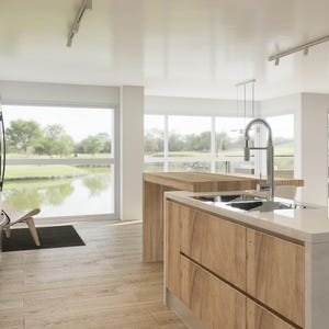 May include: A modern kitchen with a large island featuring a double sink and a chrome faucet. The island is made of light wood with a natural grain. The kitchen has large windows overlooking a golf course and a pond.