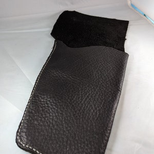May include: A black leather sleeve with a textured surface and white stitching. The sleeve is open at the top, revealing a black interior. The leather appears to be thick and durable, suitable for protecting items.