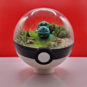 May include: A terrarium featuring a Bulbasaur figure in a miniature landscape. The clear, spherical container sits atop a white base with a black band and button detail. The background is a solid red.