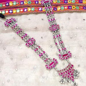 May include: A silver necklace with pink glass flowers and teardrop-shaped beads. The necklace is layered and has a dangling charm with more pink glass flowers.