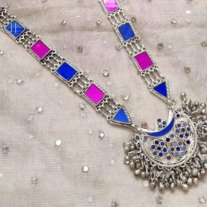 May include: A silver necklace with a crescent moon pendant decorated with blue and purple enamel. The pendant is surrounded by a fringe of silver beads. The necklace features a chain with alternating blue and pink enamel squares.